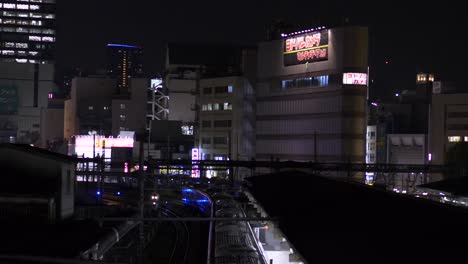 Der-Bahnhof-Ueno-Und-Die-Umliegenden-Gebäude-Bei-Nacht-Von-Einer-Fußgängerbrücke-Aus-Gesehen,-Mit-Blick-Auf-Die-Gleise-Und-Die-Vorbeifahrenden-Züge