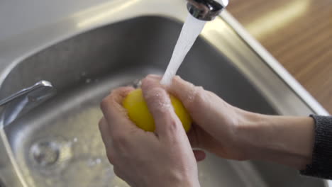 Nahaufnahme-Von-Oben-Beim-Öffnen-Des-Wasserhahns,-Dann-Händewaschen-Einer-Gelben-Zitrone-Mit-Wasser-In-Der-Küche
