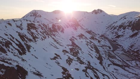 Drone-view-over-mountain-peak-in-winter-and-sun-rays