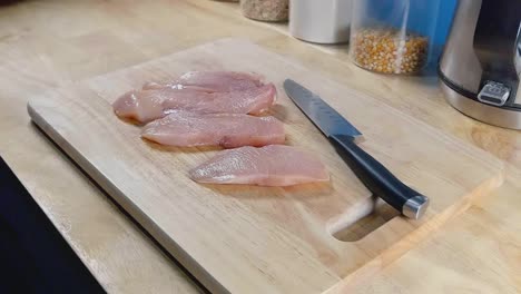 Slider-Shot-of-Chicken-Breast-Pieces-and-a-Chef's-Knife-on-a-Wooden-Cutting-Board-in-a-Home-Kitchen