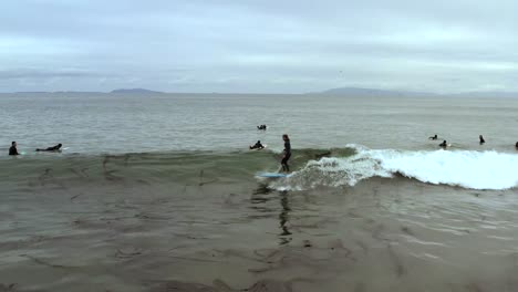 Low-aerial-view-tracking-skilled-female-surfer-riding-waves-at-Ventura-Beach