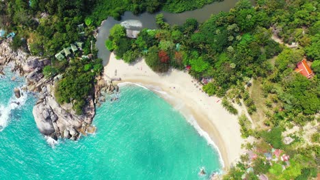 Paradise-sandy-beach-washed-by-white-waves-of-turquoise-lagoon-on-natural-harbor-with-big-cliffs,-beautiful-shore-of-tropical-island-with-lush-vegetation,-Thailand
