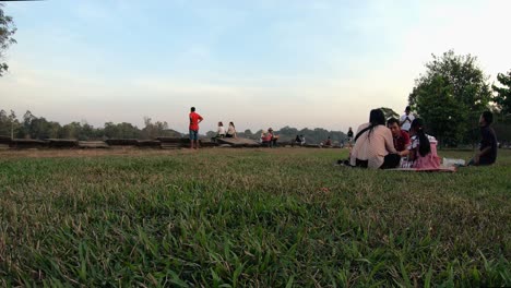 Mittlere-Außenzeitrafferaufnahme-Eines-Familienpicknicks-Auf-Dem-Rasen-Mit-Verkäufern-Und-Anderen-Leuten,-Die-Tagsüber-Bei-Angkor-Wat-Herumlaufen