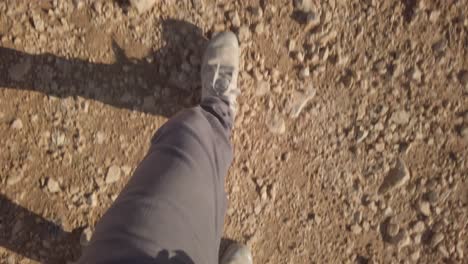 Top-view-on-feet-with-hiking-boots-walking-on-desert-ground