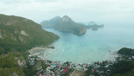 WS-AERIAL-View-of-coastal-city,-cliffs,-harbor-with-boats-and-sea,-El-Nido,-Palawan,-Philippines