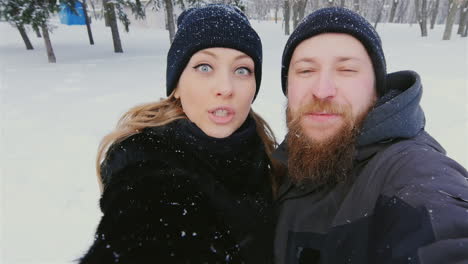 Young-Couple-Have-Fun-In-Winter-Park-Taking-Selfies