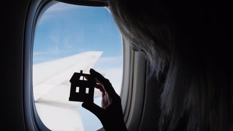 Woman-Holding-House-Figurine-by-Plane-Window