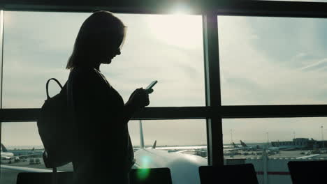 Silhouetted-Woman-Using-Smartphone-In-Airport-