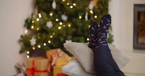 Woman-Relaxing-With-Legs-On-Cushions-Against-Christmas-Tree