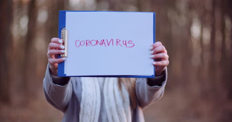 Woman-With-Protective-Mask-Holding-Coronavirus-Inscription-In-Hands-In-Forest-1