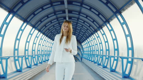 A-Stylish-Woman-Walks-Through-A-Glass-Tunnel-Listening-To-Music-On-Headphones
