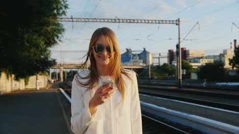 A-Business-Woman-Is-Walking-Along-The-Railway-Station-Using-A-Smartphone-Communication-In-The-Travel