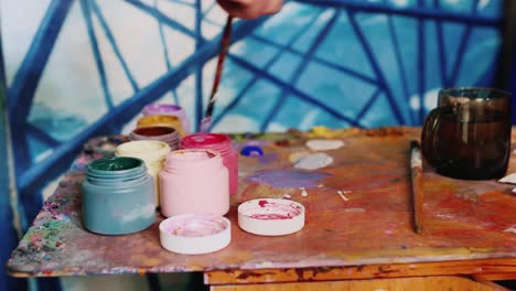 Hand-Painter-Artist-Mixes-Paint-Nearby-Stands-A-Jar-Of-Paint