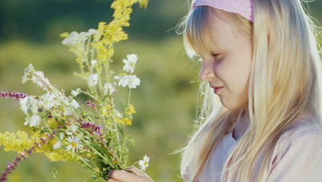 Cute-Little-Girl-Collects-Composition-From-Wild-Flowers-On-A-Background-Of-Green-Landscape