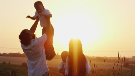 Young-Man-And-Woman-Playing-With-Young-Children-Tosses-Them-In-The-Air-Against-The-Sunset-Background