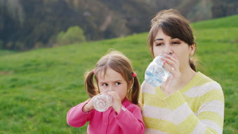 A-Young-Pretty-Woman-Drinks-Clean-Water-From-A-Plastic-Bottle-Along-With-Her-Little-Daughter