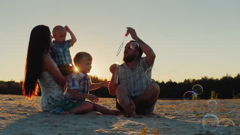 Young-Parents-And-Two-Sons-Of-The-Family-Playing-With-Soap-Bubbles-At-Sunset