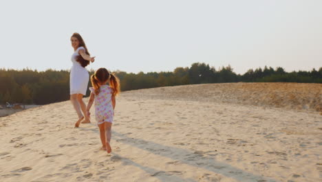Happy-Young-Mother-Playing-With-Her-Daughter-The-Girl-Runs-After-Her-Mother-On-The-Sand-At-Sunset