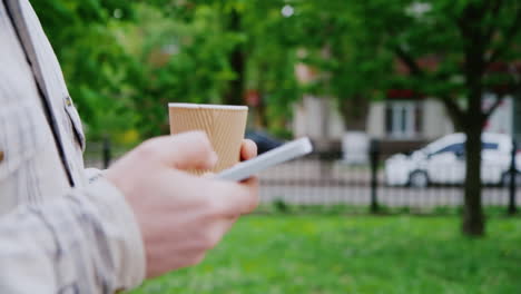 A-Man-Walks-With-The-Phone-And-Coffee-Cup-In-The-Frame-Only-Hands-Seen
