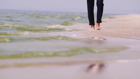 A-Barefooted-Man-In-Trousers-Walks-Along-The-Seashore-Water-Washes-His-Feet-Dream-Of-Vacation-Concep