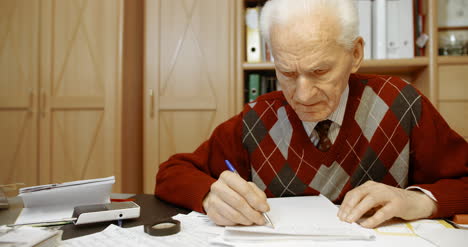 Senior-Businessman-Writing-On-Paper-At-Table-In-Office-16