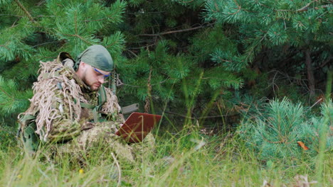 A-Man-In-Military-Uniform-Sitting-In-The-Woods-Enjoying-The-Pclaptop