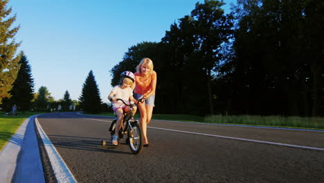 Active-Games-With-Children-Woman-Learns-The-Girl-To-Ride-A-Bike-Enjoys-The-Success-Of-A-Child