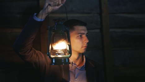 The-Frightened-Man-In-A-Suit-Standing-In-A-Dark-Room-Covers-Himself-Around-A-Kerosene-Lamp