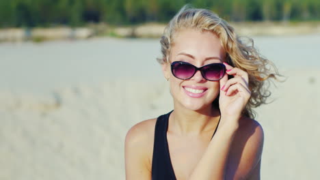 Beautiful-Young-Woman-Smiling-At-The-Camera-Looking-Over-Sunglasses-On-The-Beach-On-A-Sunny-Day