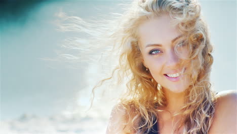 Young-Woman-Smiling-Into-The-Camera-Playing-With-Her-Beautiful-Hair-On-The-Beach-Portrait