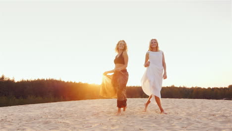 Two-Young-Women-In-Beautiful-Dresses-Are-On-The-Beach-At-Sunset-Wind-Plays-A-Beautiful-Dress-Steadic