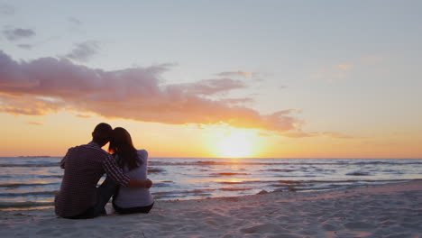 A-Young-Couple-Admiring-The-Sunset-At-Sea-Sit-In-An-Embrace-On-The-Sand-Prores-Hq-10-Bit-Video