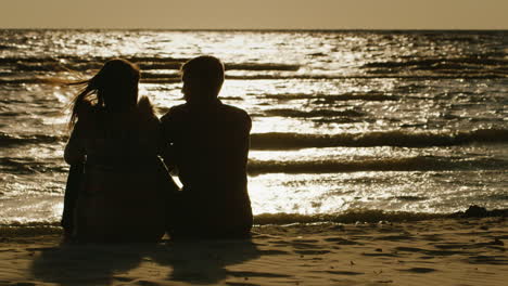 Silhouettes-Of-Couples-In-Love-Sitting-On-A-Background-Of-The-Sea-Which-Reflects-The-Setting-Sun-Rea