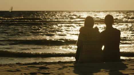 Ein-Liebevolles-Paar,-Das-Zusammen-Auf-Dem-Sand-Sitzt-Und-Das-Meer-Und-Den-Sonnenuntergang-Bewundert