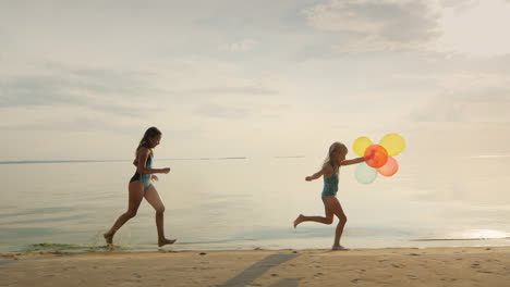 Two-Sisters-Playing-Together-On-The-Beach-One-Girl-Runs-After-Another-Holding-Balloons-Slow-Motion-S