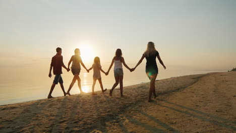 Group-Of-Children-Of-Different-Ages-With-Adults-Are-On-The-Beach-At-Sunset-Holding-Hands-Rear-View-S