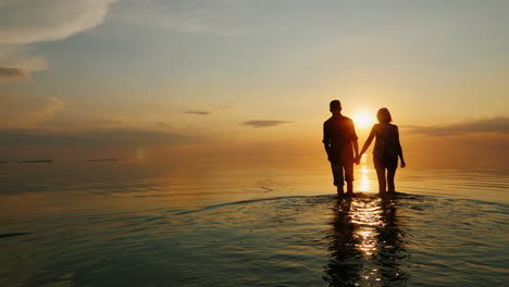 A-Man-And-A-Woman-Go-To-The-Sea-At-Sunset-Holding-Hands-Silhouettes-In-The-Light-Of-The-Setting-Sun