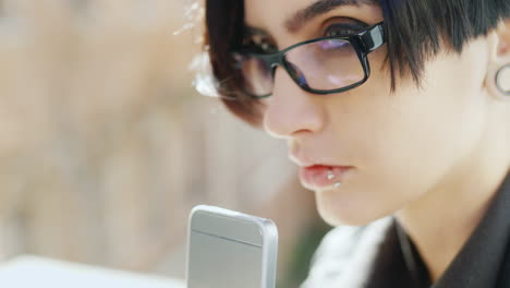 Close-Up-Of-Attractive-Brunette-In-Hipster-Glasses-Is-Typing-On-A-Mobile-Phone-Her-Hands-With-The-Ph