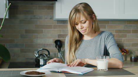 Young-Attractive-Woman-Reading-A-Book-In-The-Kitchen-Nearby-Stands-A-Glass-Of-Milk-Concept---Healthy