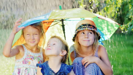 Three-Cheerful-Carefree-Girl-Under-The-Umbrella-Of-The-Rainbow-Colors-There-Is-A-Warm-Rain-Happy-Chi