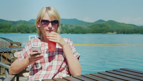 Woman-Resting-On-A-Summer-Area-In-The-Cafe-It-Uses-The-Phone-In-The-Background-The-Lake-And-The-Moun