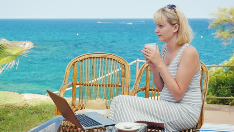 Junge-Frau,-Die-Kaffee-Trinkt,-Sitzt-Auf-Der-Terrasse-Mit-Blick-Auf-Das-Meer-Neben-Dem-Laptop-Perfekt-Für