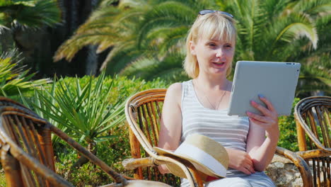 Woman-Tourist-With-The-Tablet-Says-He-Sits-In-A-Wicker-Chair-On-The-Background-Of-Palm-Trees-Always-