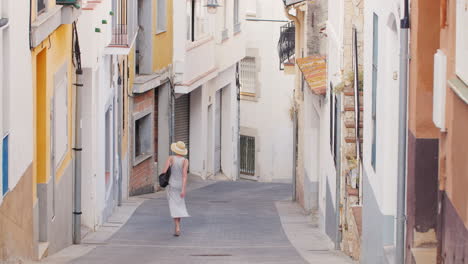 Woman-Tourist-In-Light-Dress-And-Hat-Goes-Down-The-Narrow-Streets-Of-The-Old-Mediterranean-City-In-S
