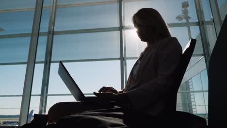 Silhouette-Of-A-Business-Woman-With-A-Laptop-Working-In-Anticipation-Of-Her-Flight-Sits-By-The-Large