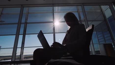 Silhouette-Of-A-Business-Woman-With-A-Laptop-Working-In-Anticipation-Of-Her-Flight-Sits-By-The-Large