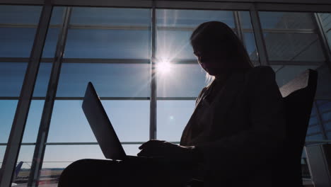 Silhouette-Of-A-Man-Using-A-Laptop-Near-A-Large-Window-In-The-Airport-Terminal