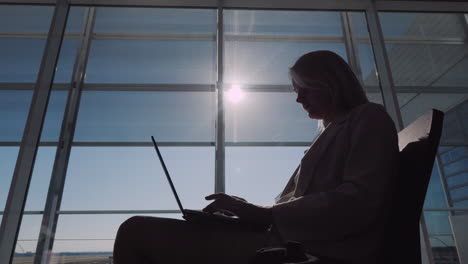 Silhouette-Einer-Jungen-Geschäftsfrau,-Die-Mit-Einem-Laptop-In-Der-Flughafenlobby-Auf-Ihren-Flug-Wartet