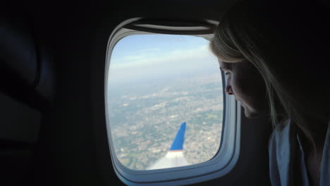 A-Young-Female-Passenger-Looks-Out-Of-The-Window-Of-The-Plane-To-The-Ground-Far-Below-Where-The-Metr