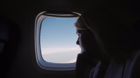 Silhouette-Of-A-Young-Woman-Flying-In-An-Airplane-Looking-Out-The-Window